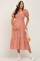 woman wearing a red and white gingham maternity dress with puff sleeves and a tiered skirt, holding her baby bump