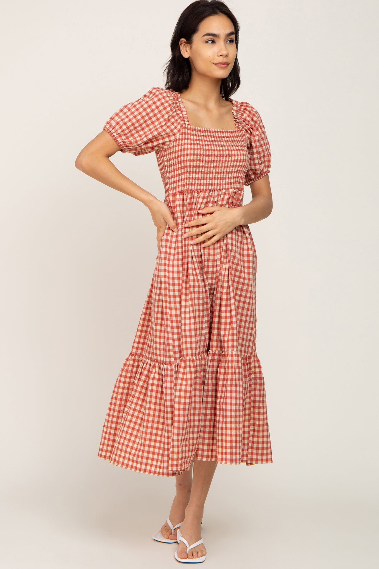 woman wearing a red and white checkered midi dress with puff sleeves and a tiered skirt, standing sideways