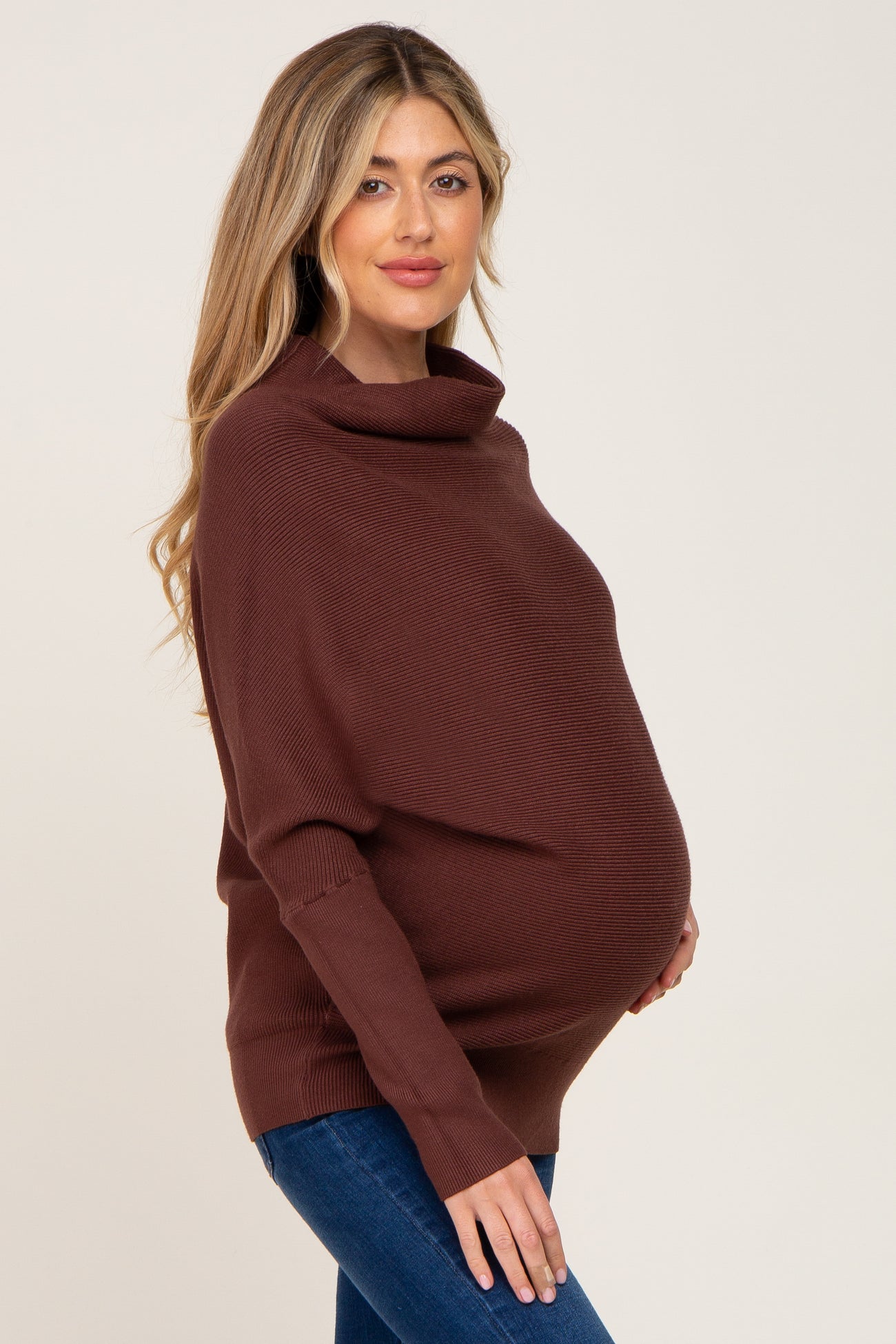 Pregnant woman wearing a brown ribbed cowl neck maternity sweater and blue jeans