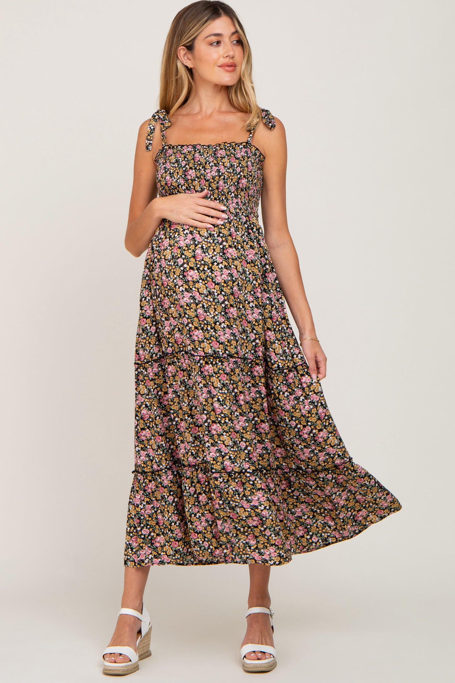 Pregnant woman wearing a floral smocked maternity midi dress with tie straps and white wedge sandals