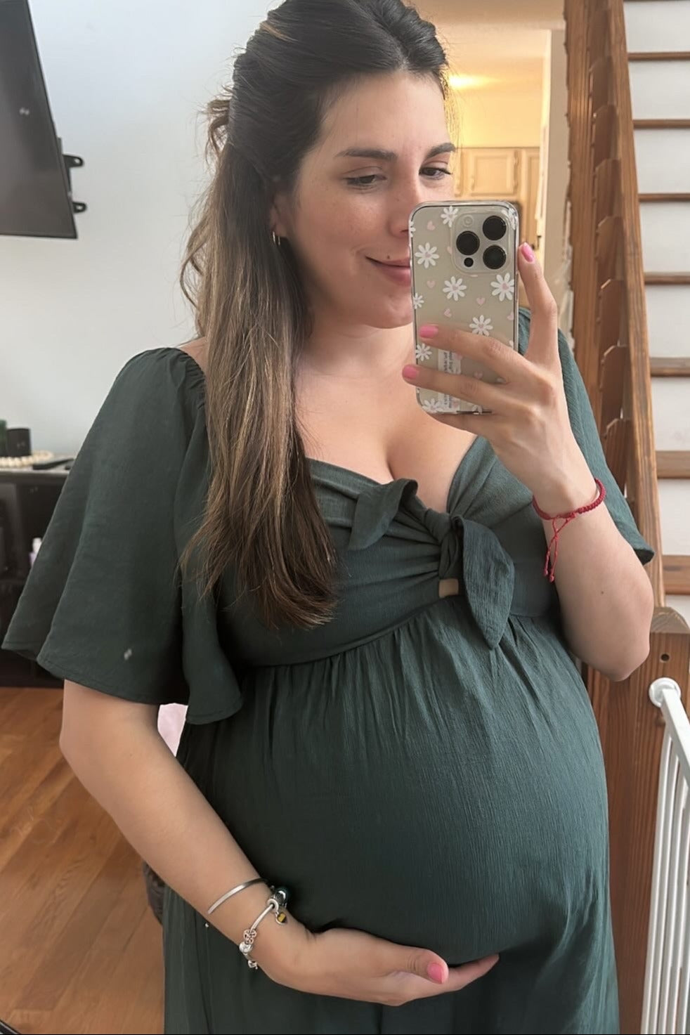 woman wearing a dark green maternity dress with a tie front and flutter sleeves, holding her baby bump
