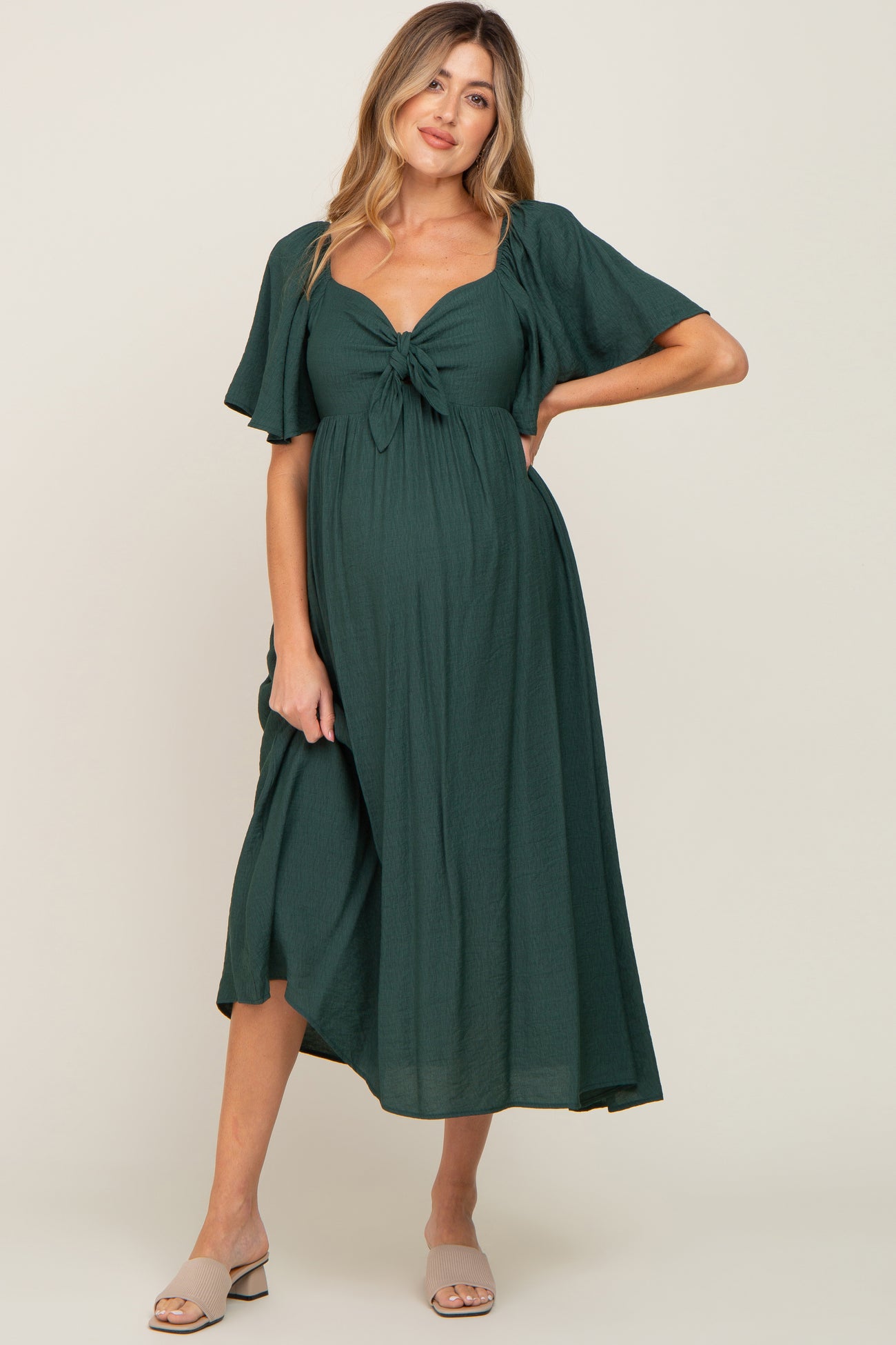 woman wearing a dark green maternity dress with a knotted front and flutter sleeves, showcasing her baby bump