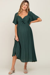 woman wearing a dark green maternity dress with a knotted front and flutter sleeves, showcasing her baby bump