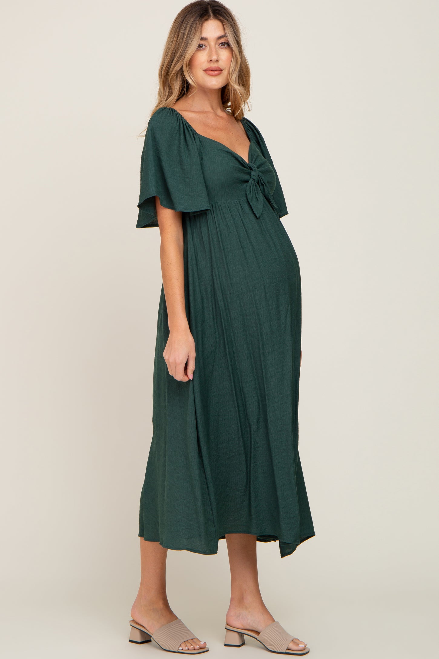 woman wearing a dark green maternity dress with a tie front and flutter sleeves, showcasing her baby bump