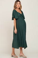 woman wearing a dark green maternity dress with a tie front and flutter sleeves, showcasing her baby bump