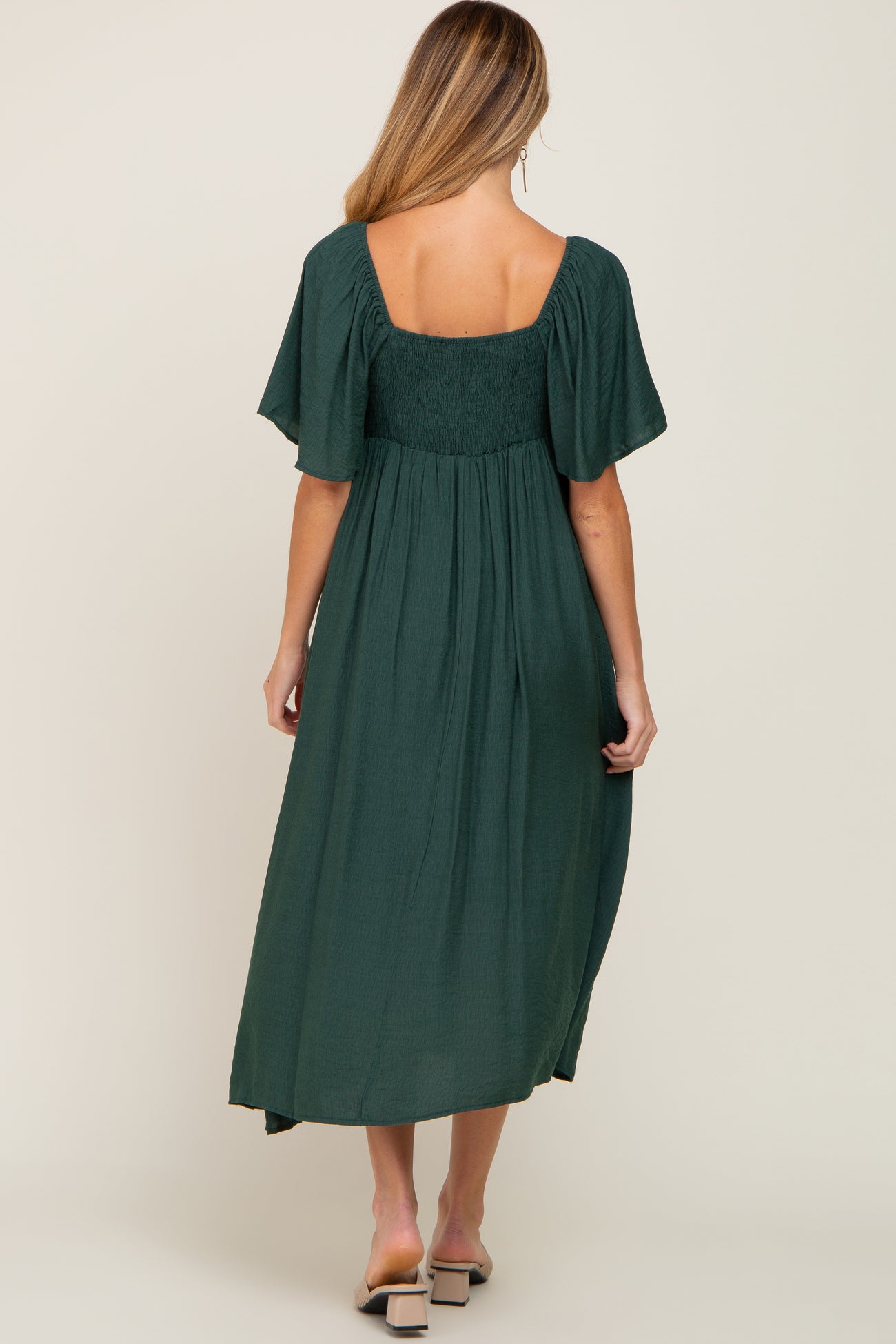 woman wearing a dark green maternity maxi dress with short sleeves and a smocked bodice, showing her baby bump