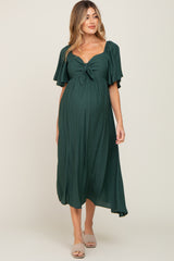 woman wearing a dark green maternity dress with a tie front and flutter sleeves, showcasing her baby bump