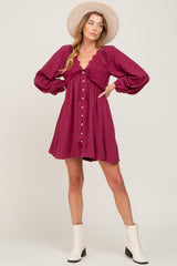 woman wearing a burgundy long sleeve mini dress with a lace detail and buttons, paired with white ankle boots and a hat