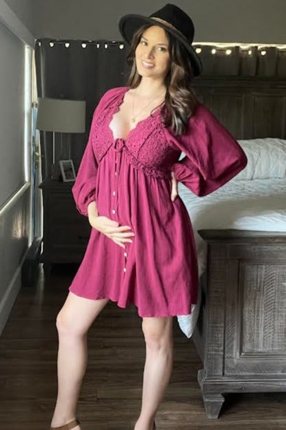 woman wearing a burgundy maternity dress with button front and puff sleeves, holding her baby bump