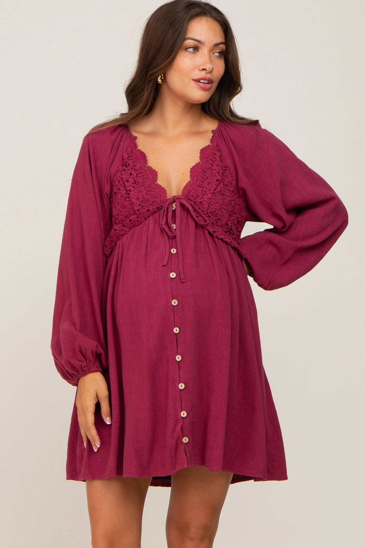 woman wearing a burgundy maternity dress with crochet detailing, long sleeves, and button closure, showing her baby bump