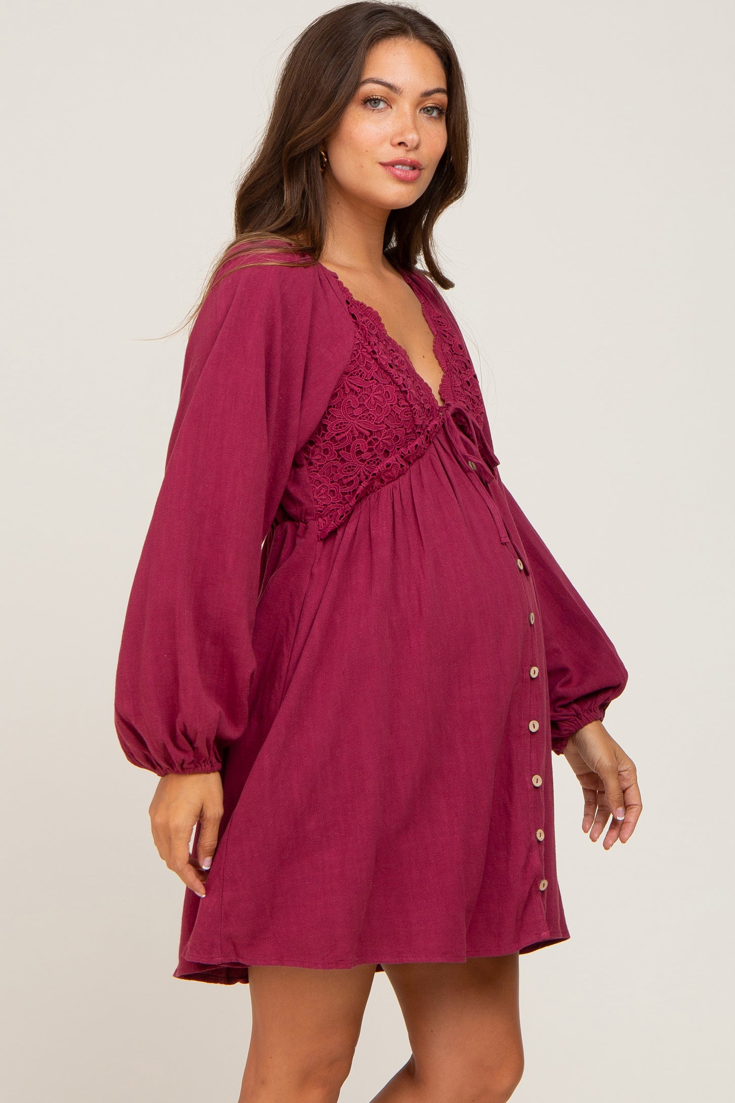 woman wearing a burgundy maternity dress with lace details and buttons, showing her baby bump