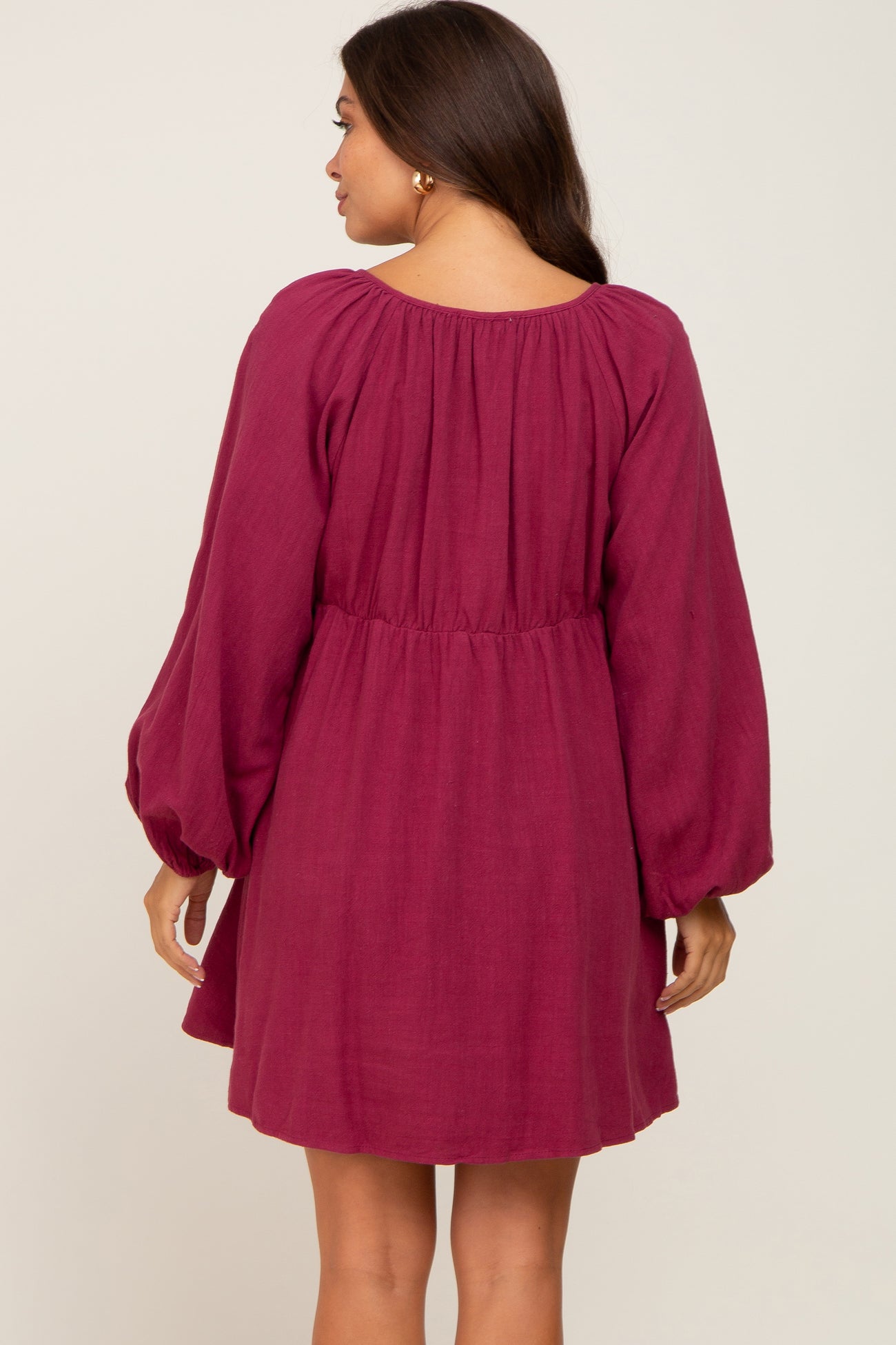 woman wearing a plum colored maternity dress with long puff sleeves and a cinched waist seen from the back