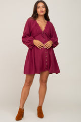 woman wearing a burgundy maternity dress with a lace detail and button closure, holding her baby bump