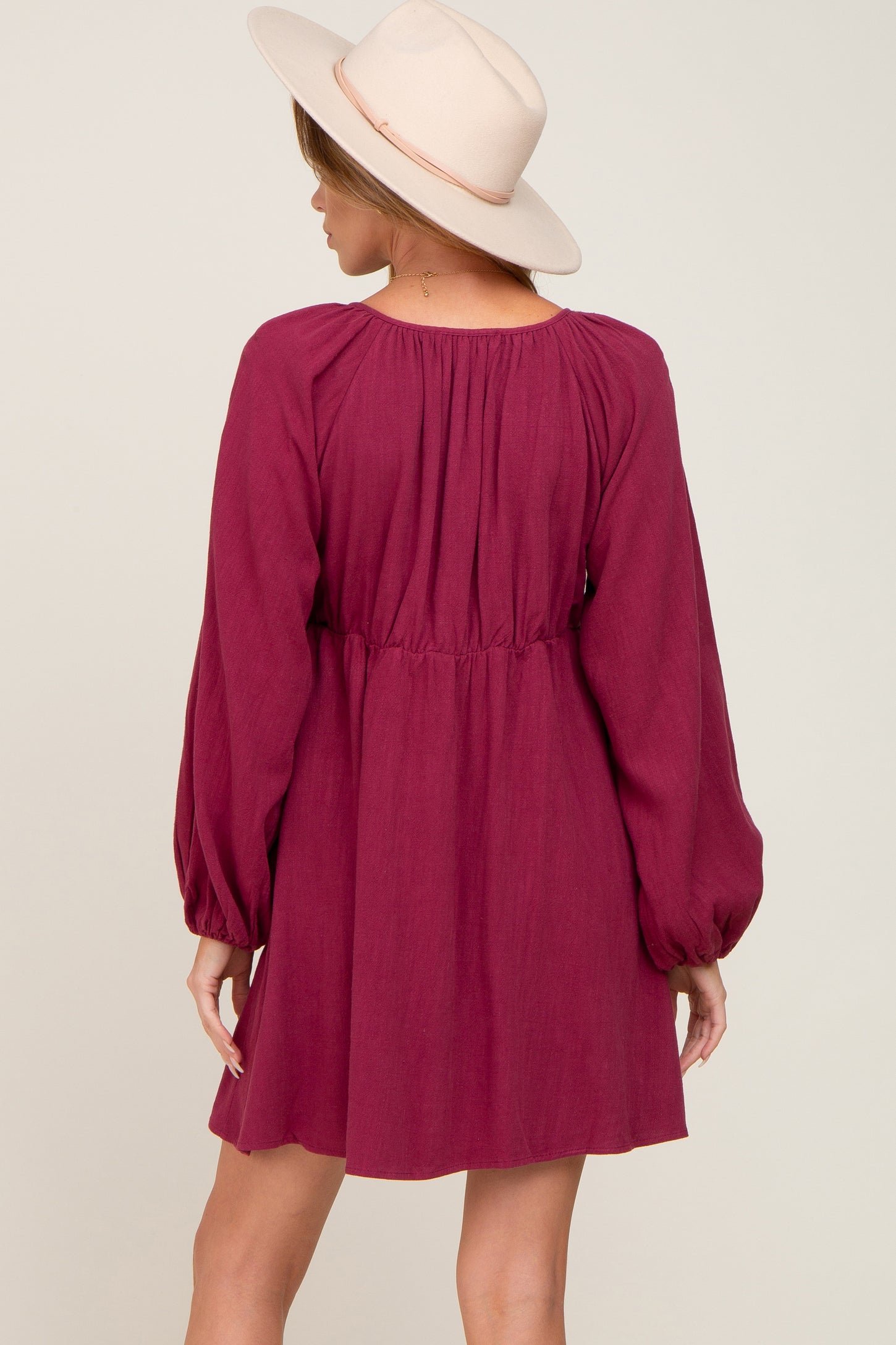 woman wearing a maroon long sleeve dress with a cinched waist and flowing sleeves, paired with a light beige hat