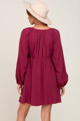 woman wearing a maroon long sleeve dress with a cinched waist and flowing sleeves, paired with a light beige hat