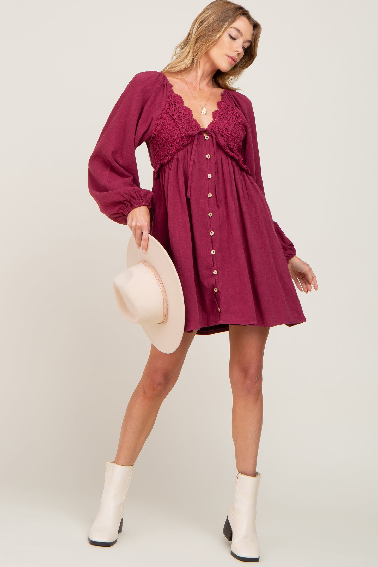 woman wearing a burgundy long sleeve button-up dress with lace details, paired with a beige hat and white ankle boots