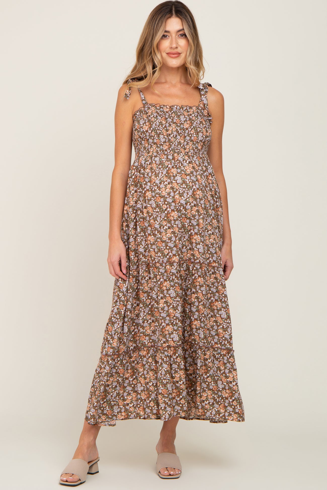 woman wearing a brown floral maternity maxi dress with adjustable straps and a ruffled hem, showcasing her baby bump
