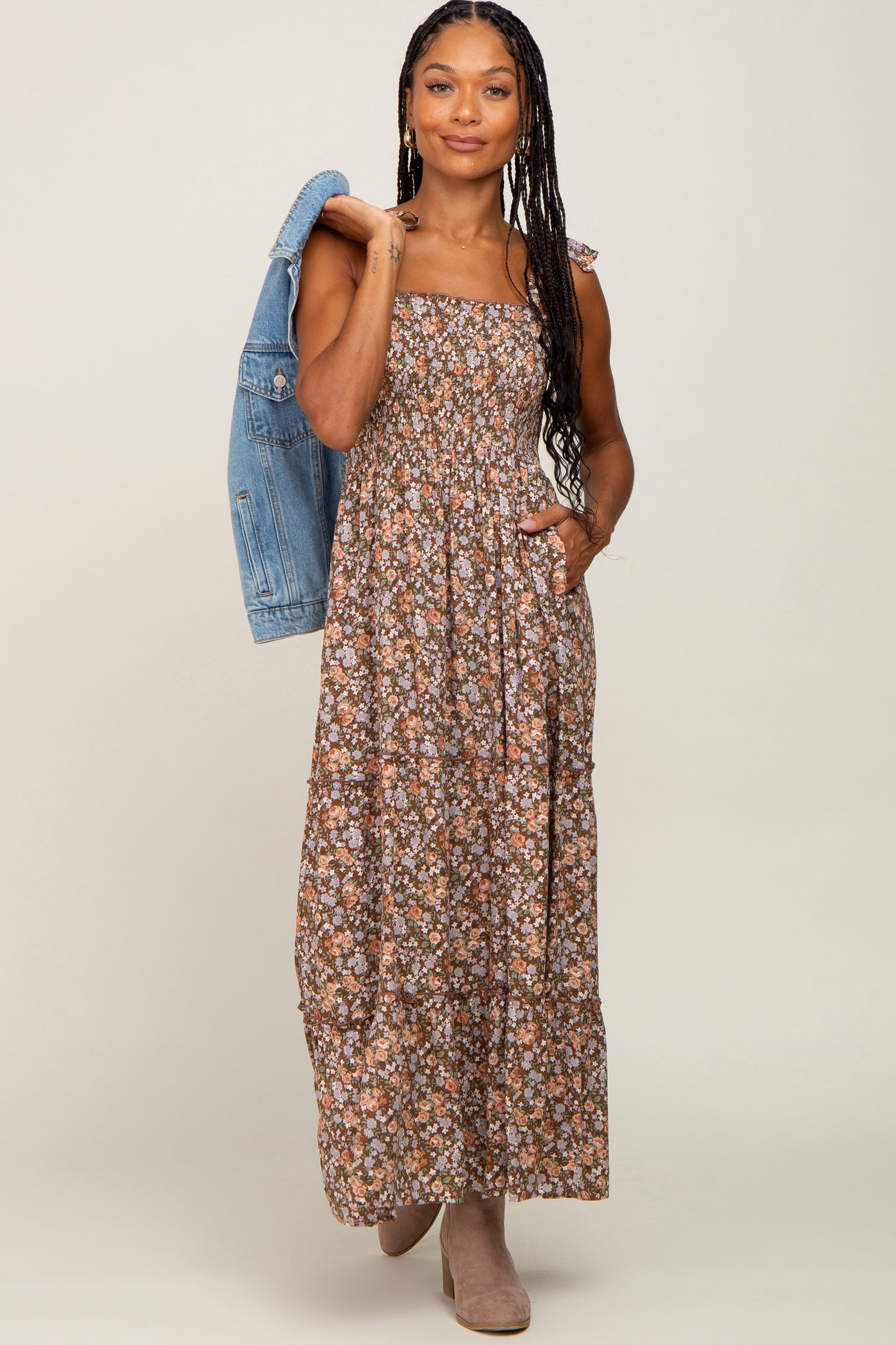woman wearing a brown floral maxi dress with spaghetti straps and pockets, paired with a denim jacket and ankle boots