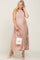 woman wearing a blush pleated maternity gown with a tie waist and holding a handbag while showcasing her baby bump