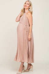 woman wearing a light pink pleated maternity dress with a halter neck and tie waist, showing her baby bump