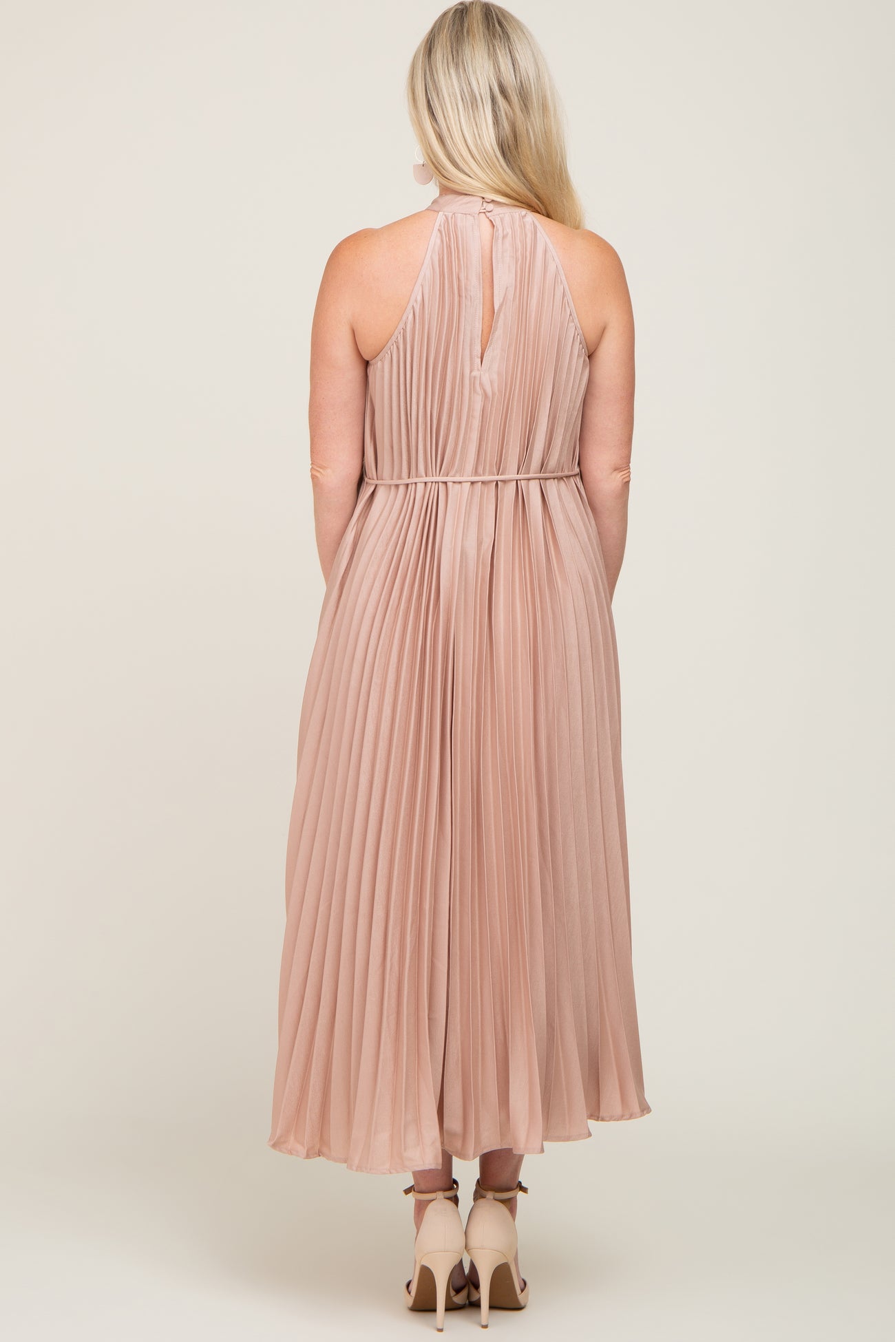 woman wearing a blush pleated maternity dress with a halter neck and a flowing silhouette from the back