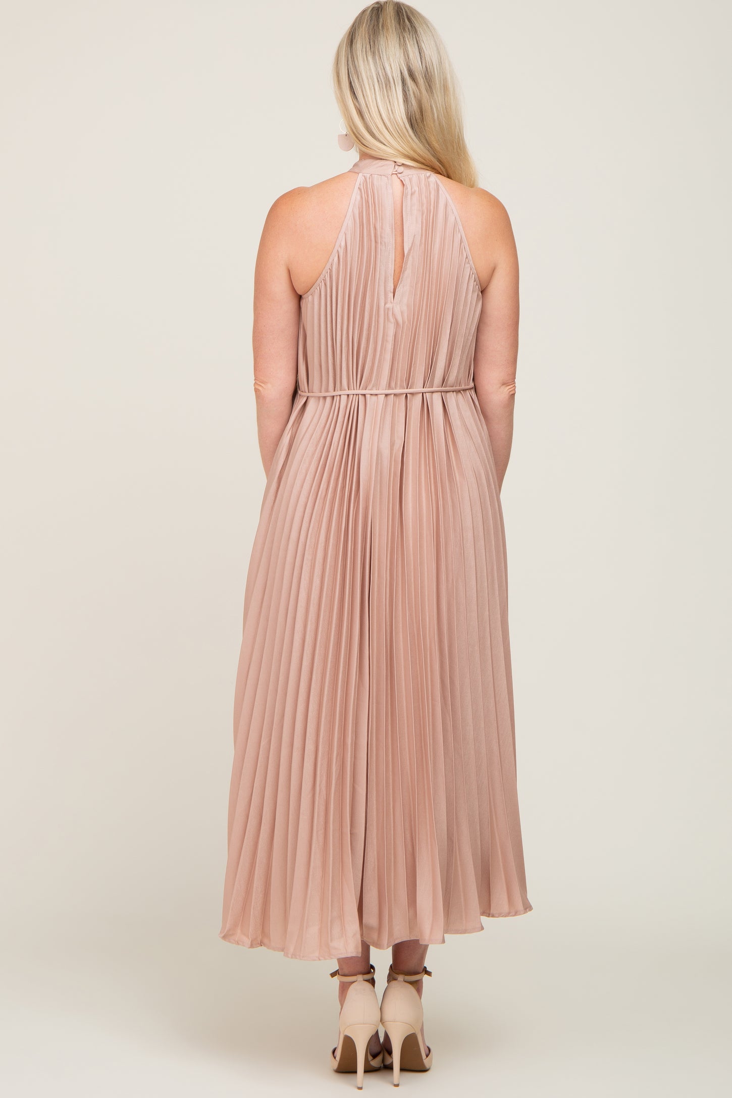 woman wearing a blush pleated maternity dress with a halter neck and a flowing silhouette from the back