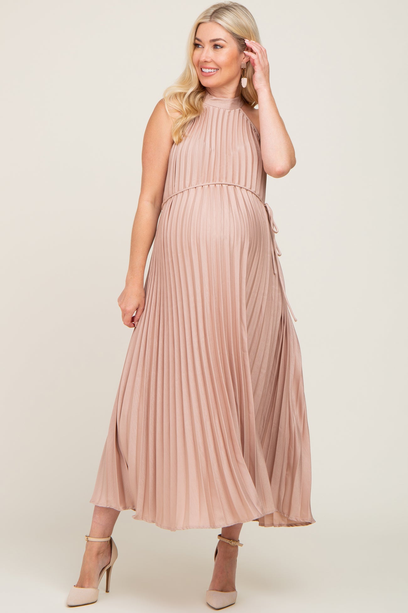 woman wearing a light pink pleated maternity dress with a tie waist and a visible baby bump