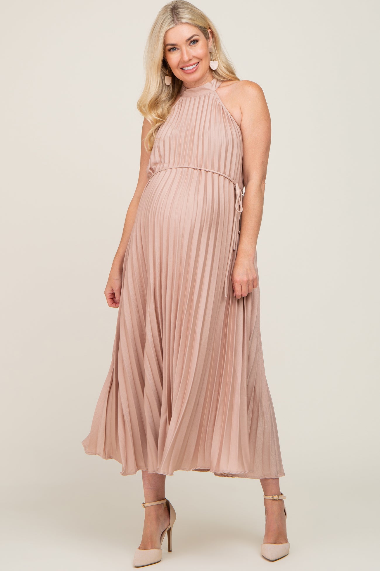 woman wearing a blush pleated maternity dress with a halter neckline and a baby bump visible