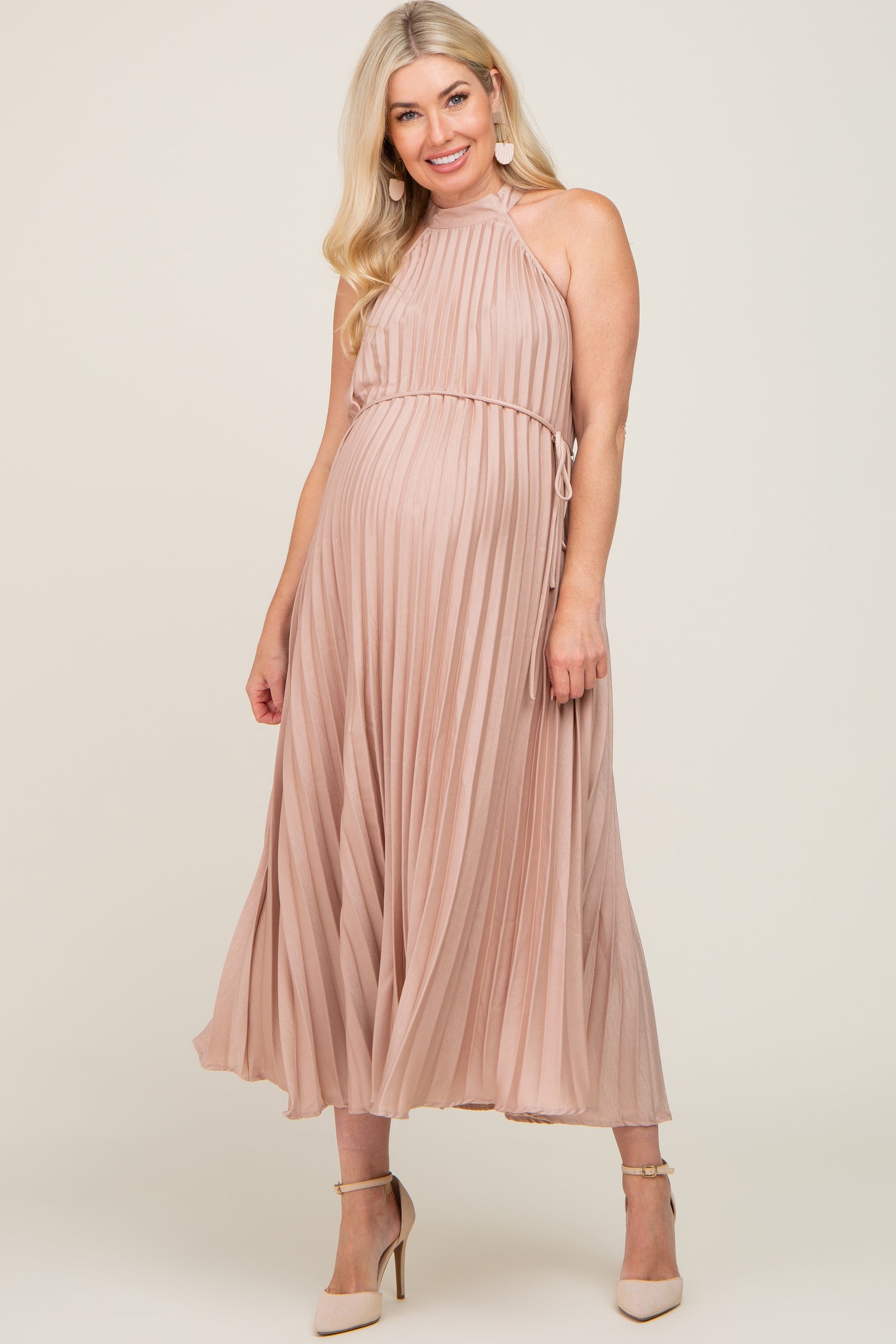 woman wearing a blush pleated maternity dress with a halter neckline and a baby bump visible
