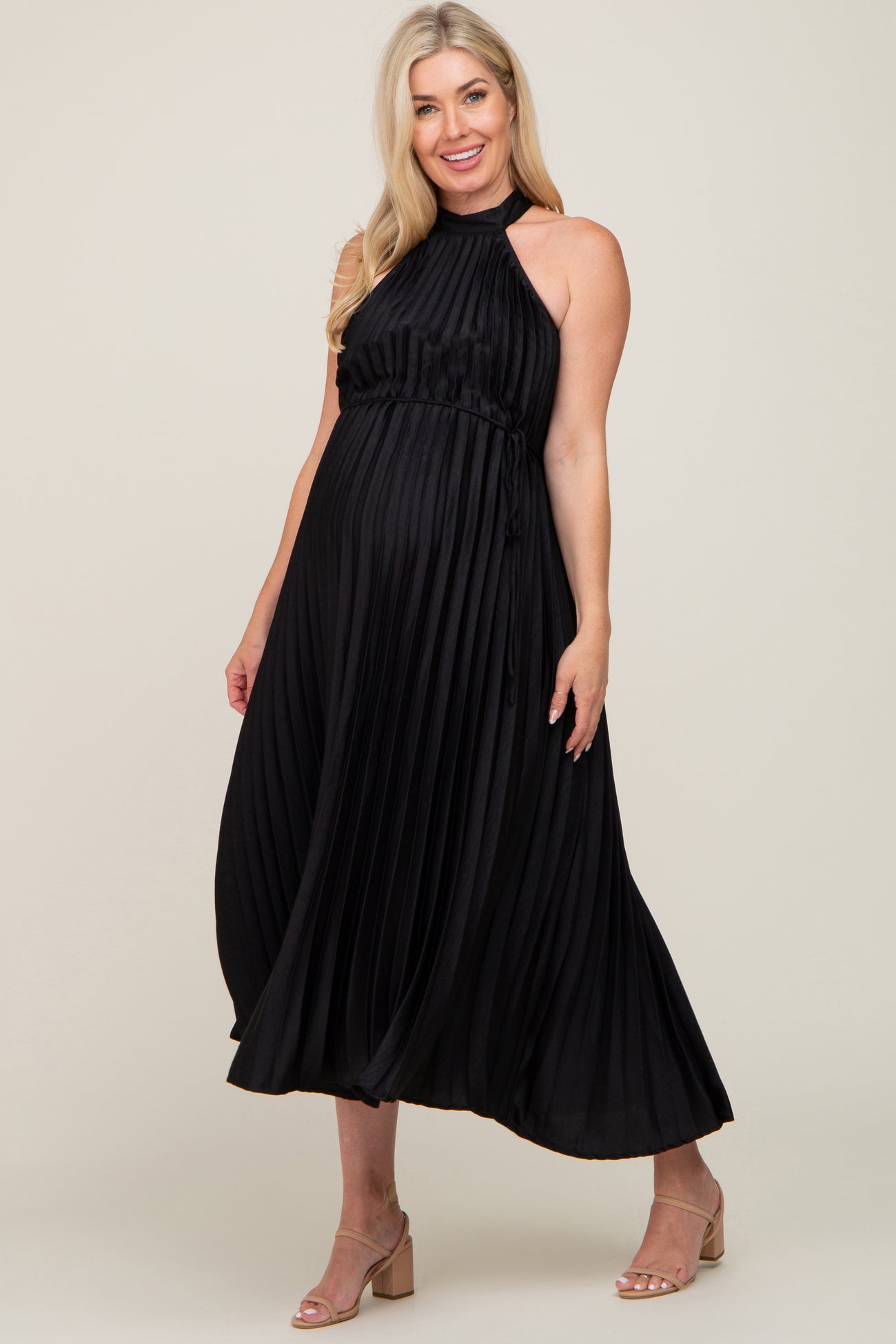 woman wearing a black pleated maternity dress with a halter neckline and adjustable tie, highlighting her baby bump