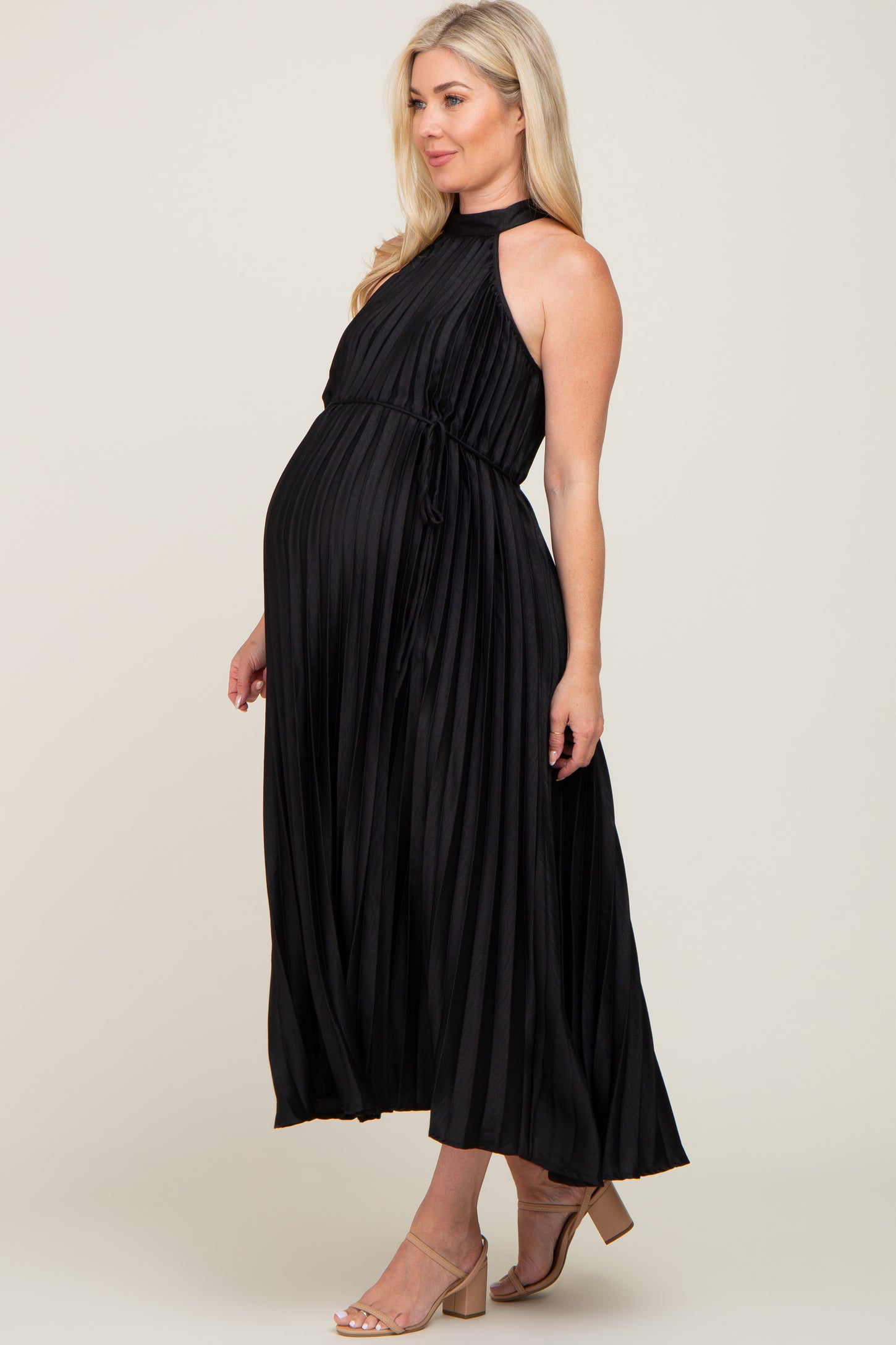woman wearing a black pleated maternity maxi dress with a halter neckline and a tied waist, showing her baby bump