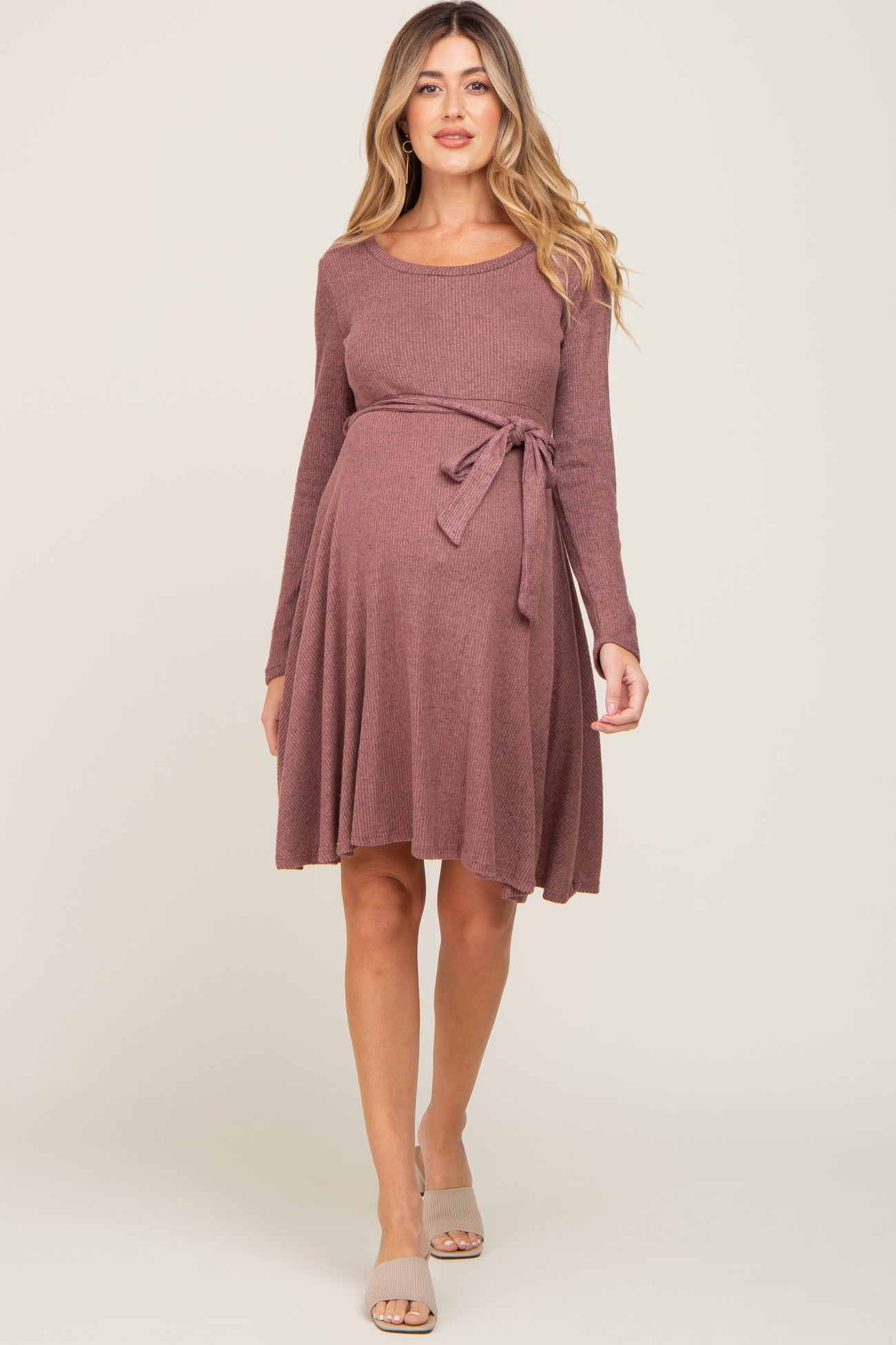 woman wearing a mauve long sleeve maternity dress with a tie waist and flared skirt, showcasing her baby bump