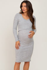 woman wearing a grey long sleeve maternity dress with a crossover design and holding her baby bump