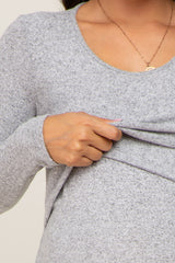 woman wearing a gray long sleeve maternity top, lifting the fabric to reveal a nursing function.