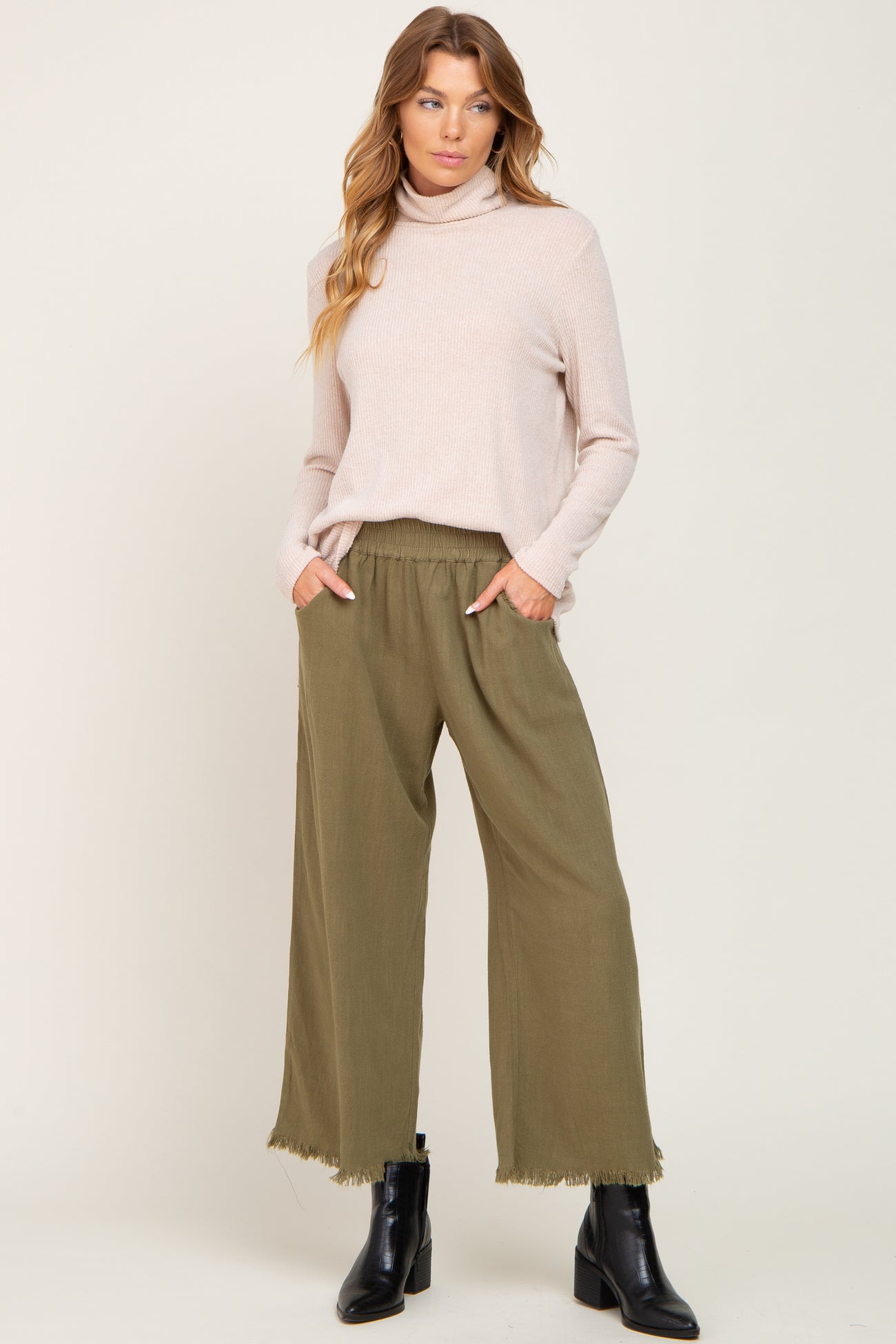 woman wearing a light pink turtleneck sweater and olive green wide-leg pants with frayed edges