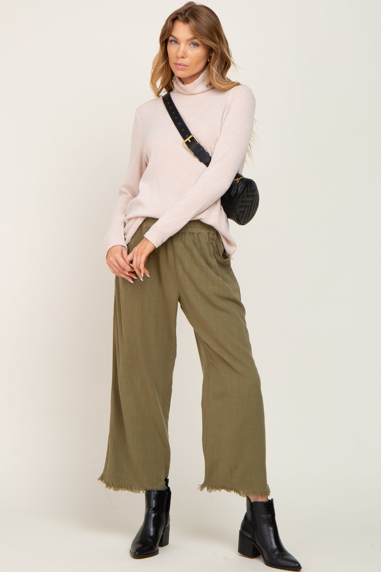 woman wearing a light pink turtleneck sweater with olive green wide-leg pants and black ankle boots