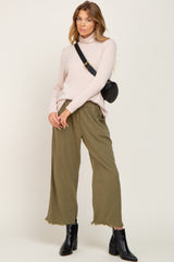 woman wearing a light pink turtleneck sweater with olive green wide-leg pants and black ankle boots
