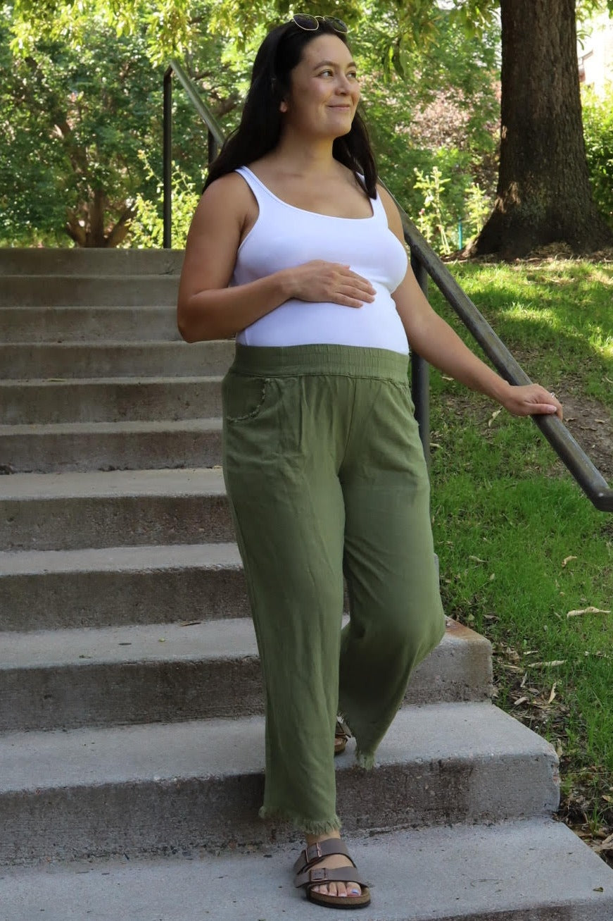 woman wearing a white tank top and green maternity pants, showing her baby bump while walking down steps outdoors