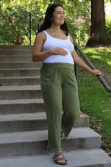 woman wearing a white tank top and green maternity pants, showing her baby bump while walking down steps outdoors