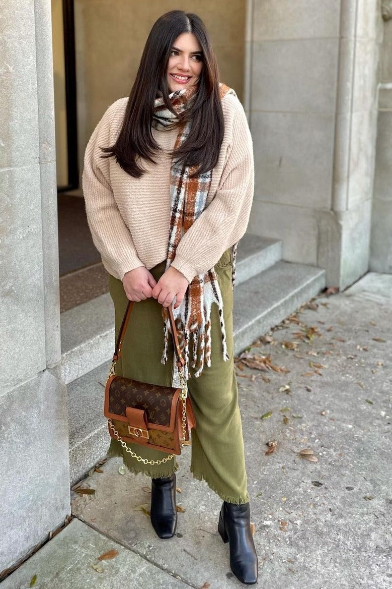 woman wearing a beige oversized sweater and olive green skirt, accessorized with a plaid scarf and carrying a brown handbag