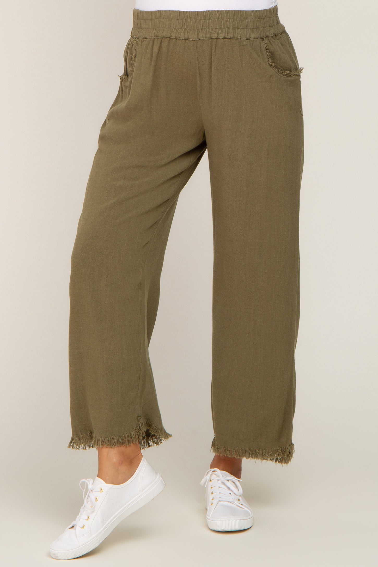 woman wearing olive green maternity pants with an elastic waistband and fringed hem, paired with white sneakers