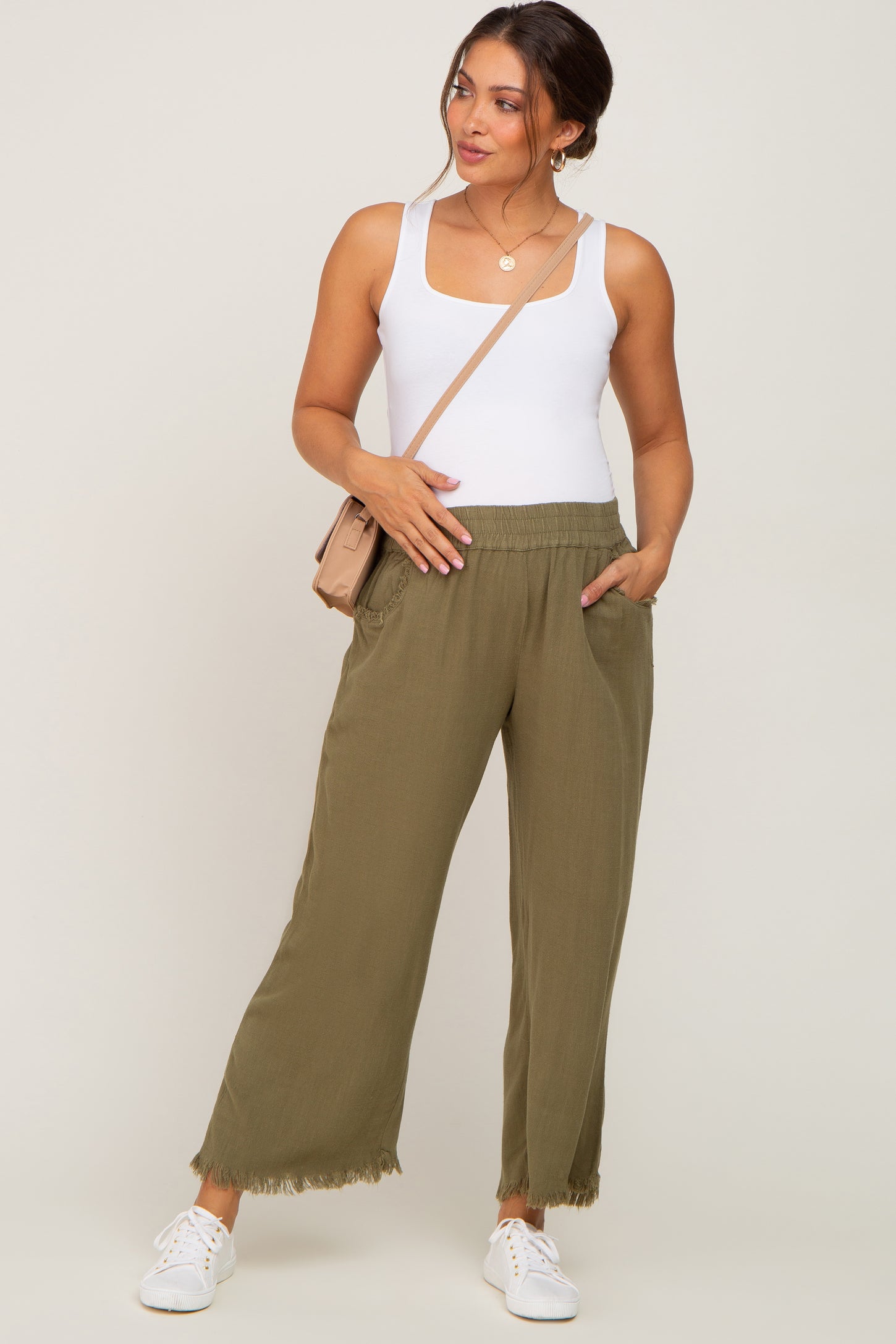 woman wearing olive green wide-leg maternity pants with pockets and a white fitted tank top, holding her baby bump