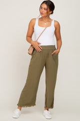 woman wearing olive green wide-leg maternity pants with pockets and a white fitted tank top, holding her baby bump