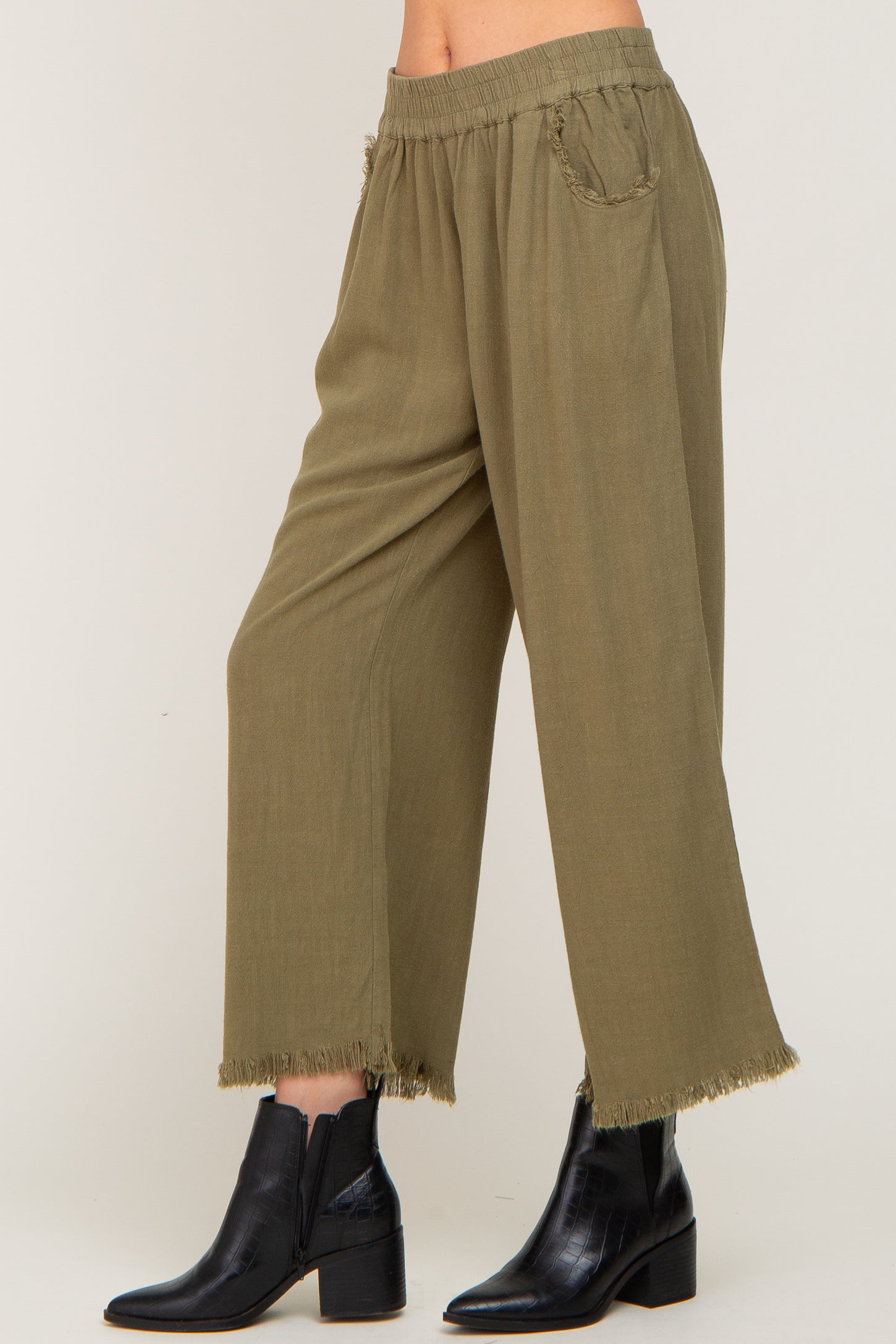 woman wearing olive green wide-leg pants with frayed hem and elastic waistband, paired with black ankle boots