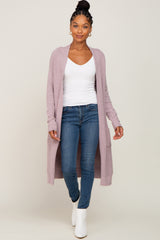 woman wearing a light purple long cardigan over a white top and blue jeans, walking in white ankle boots