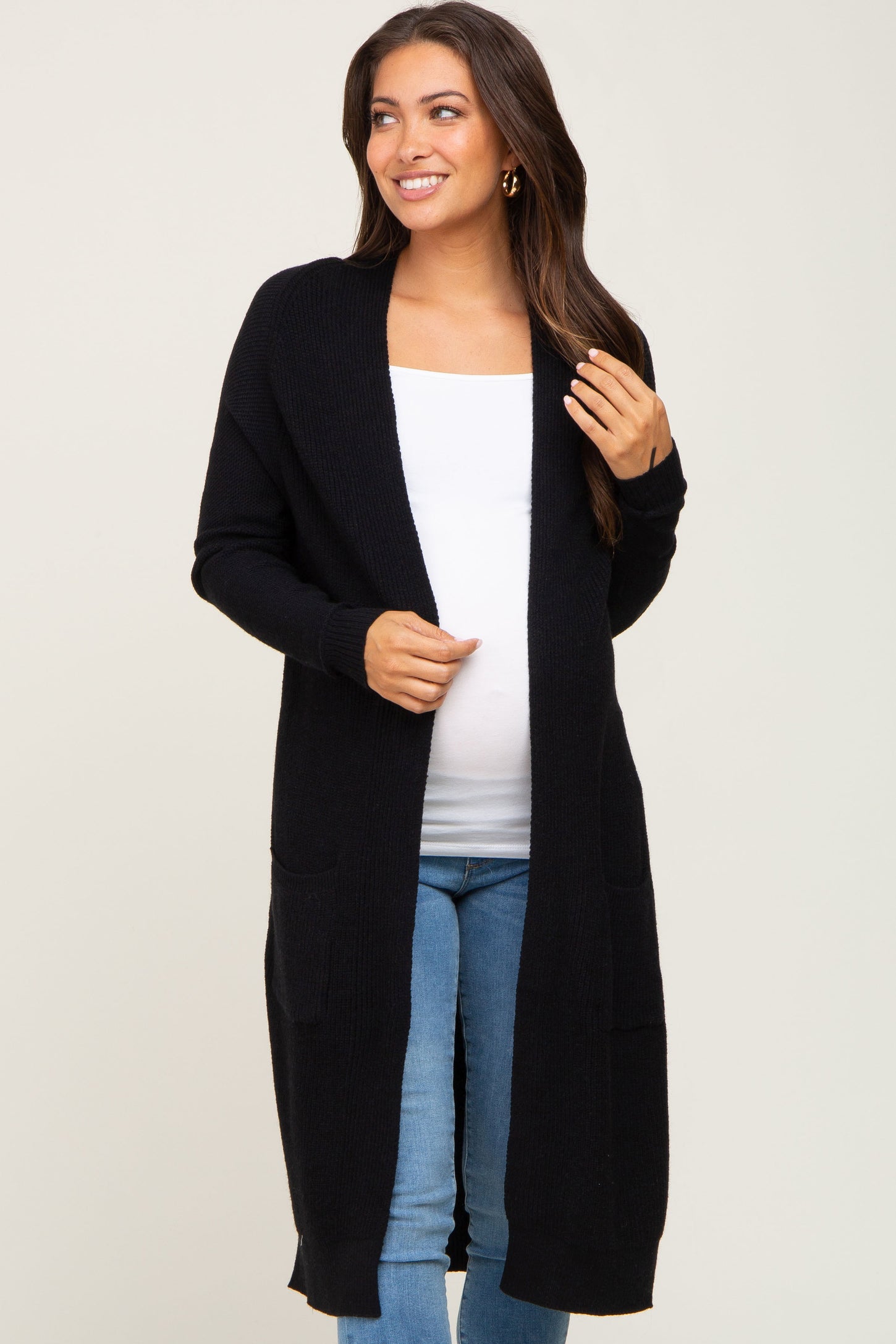 woman wearing a black long sleeve maternity cardigan over a white top and showing her baby bump, styled with jeans