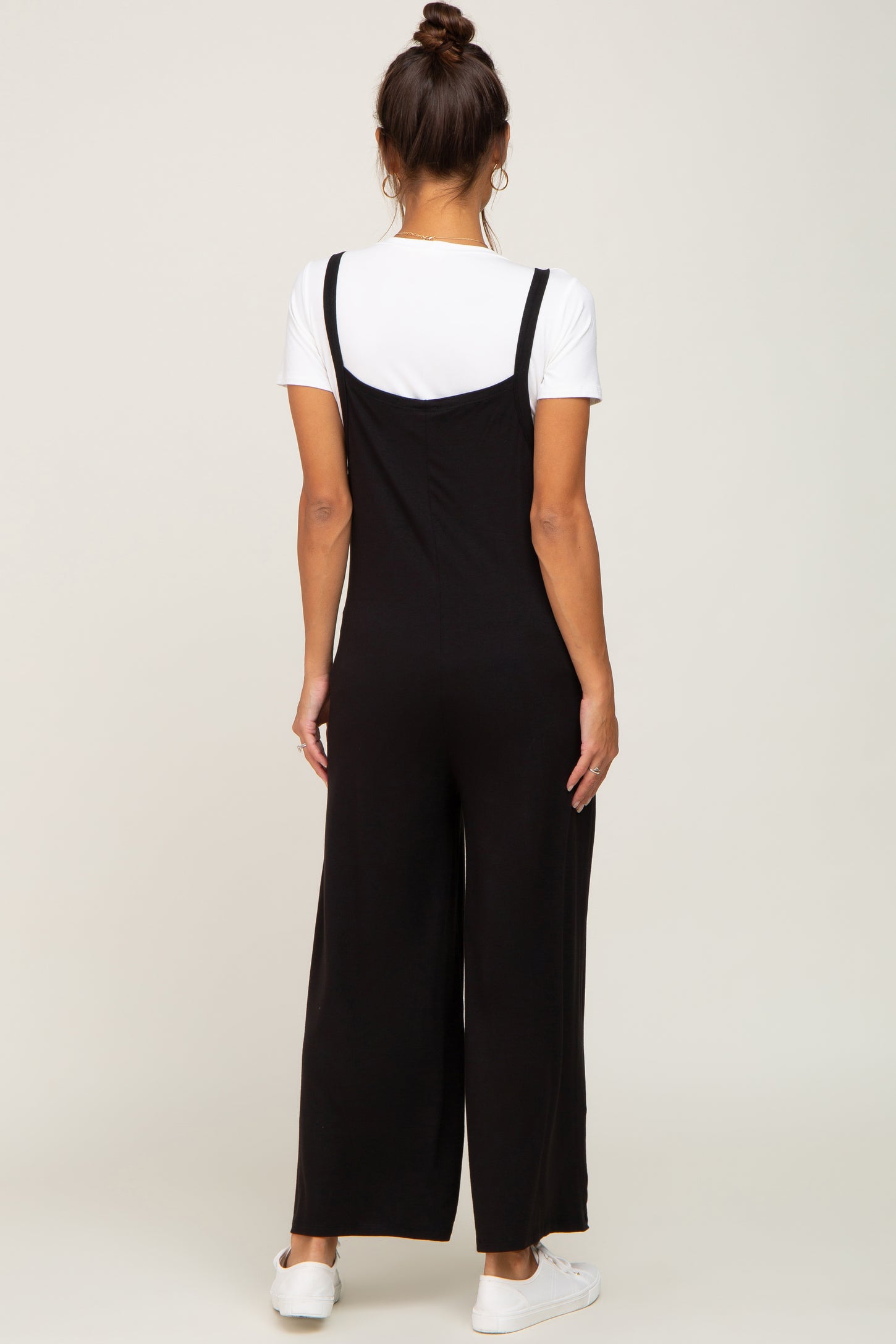 woman wearing a black maternity jumpsuit with a white t-shirt underneath, seen from the back