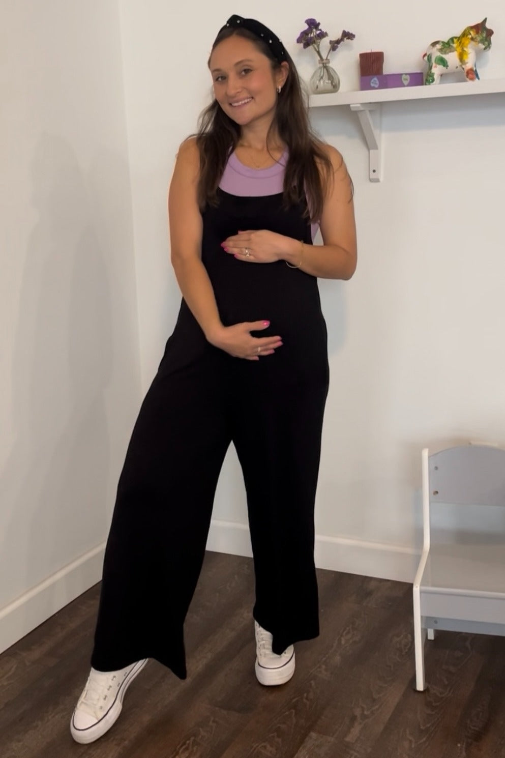 woman wearing a black maternity overall with a lavender top and holding her baby bump