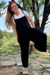 woman wearing a black maternity jumpsuit with a white t-shirt underneath and a headband, showing her baby bump