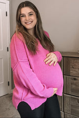 woman wearing a hot pink oversized maternity sweater and holding her baby bump